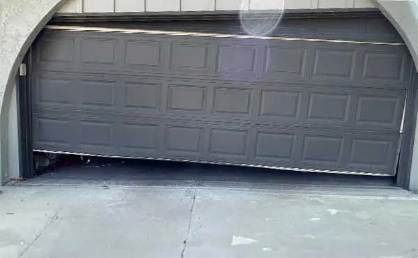 Broken garage door partly open and crooked
