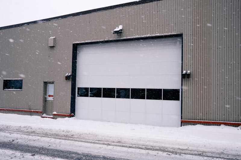 Snowy warehouse exterior with closed garage door.