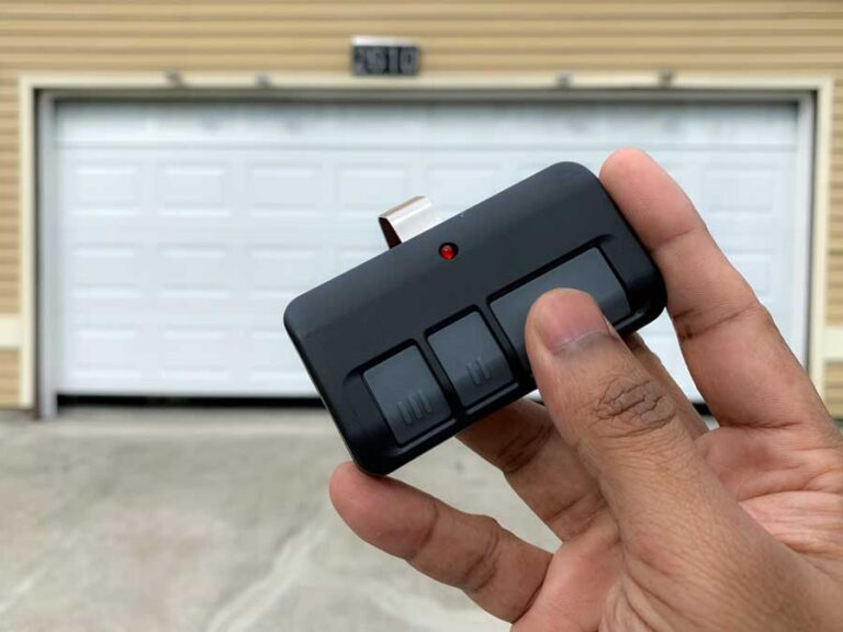 Hand holding garage door remote in front of garage.
