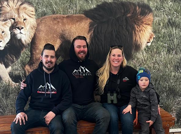 Family posing with lion background at a zoo.