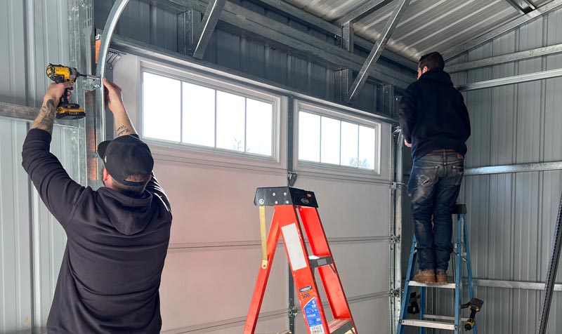 Two workers repairing a garage door inside.