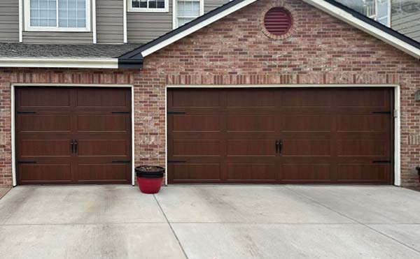 Two brown garage doors on brick house.
