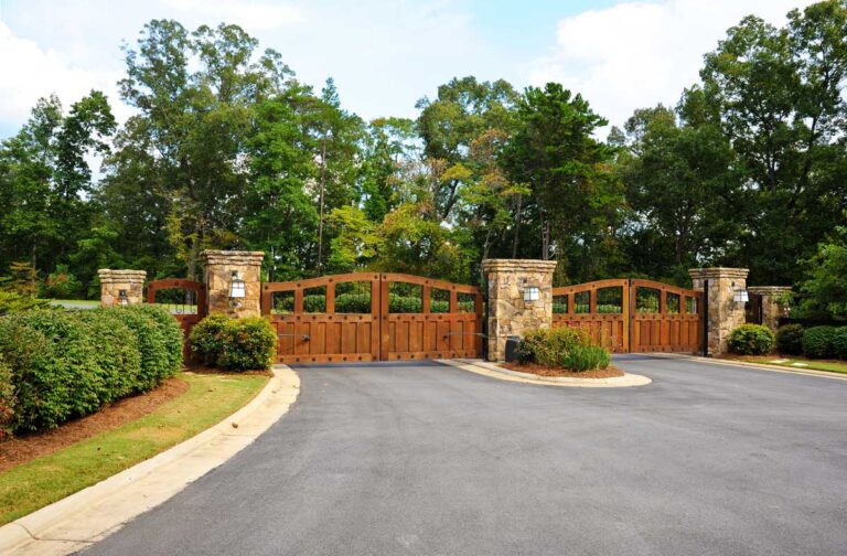 Elegant wooden gate with stone pillars and trees.